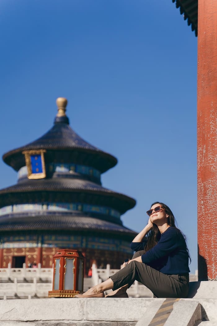 Mujer sentada con gafas de sol a tras de ella está un edificio ancestral en Beijing China