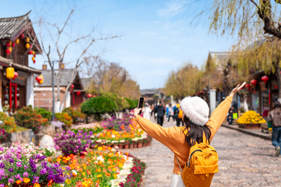 Chica feliz con los brazos extendidos frente a una calle colorida en un día soleado en Yunnan China